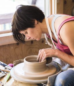 Profile picture of Sarah Lindley leaning over a pottery wheel